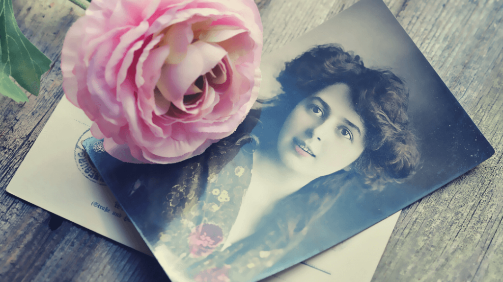 Altes-Foto-einer-jungen-Frau-auf-einer- Postkarte-zusammen-mit-einer-rosafarbenen-Rose.