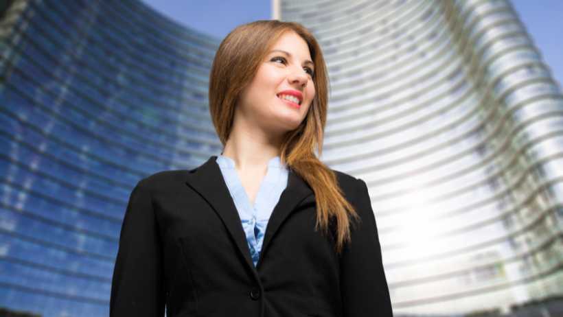 Frau-im-business-outfit-vor-einem-glasgebäude-bei-blauem-himmel